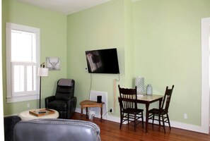 Una sala de estar con televisor, una silla, una mesa y un sofá.