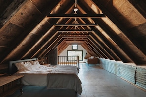 An attic bedroom with a sloped ceiling, a bed, a small table, and a view of the outside through a window. - Secluded and Rustic Three Bedroom Cabin with Wood Burning Stove, Perfect for a Glamping Retreat in the Sequoias (Dunlap)