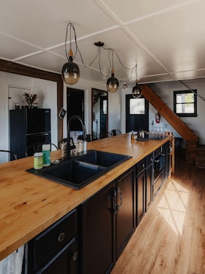A kitchen with a wooden island, black appliances, and pendant lighting. - Secluded and Rustic Three Bedroom Cabin with Wood Burning Stove, Perfect for a Glamping Retreat in the Sequoias (Dunlap)