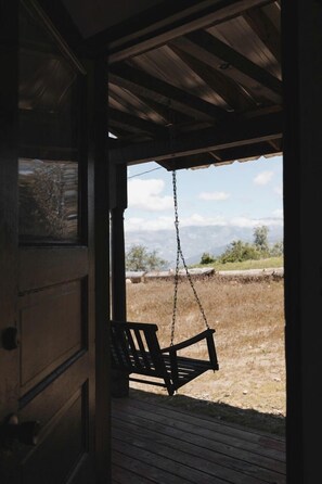 Eine hölzerne Veranda mit einem Schaukelstuhl, einer Tür und Blick auf eine Landschaft mit Bergen.