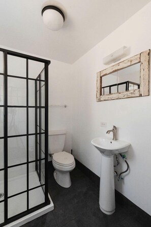 Un baño con cabina de ducha de vidrio, inodoro blanco y lavamanos pedestal.