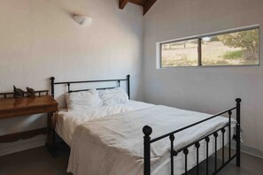 A bedroom with a bed, a wooden nightstand, a wall-mounted light, and a window with a view of the outdoors. - Secluded and Minimalist One Bedroom Cabin, Perfect for a Visit to Kings Canyon National Park (Dunlap)
