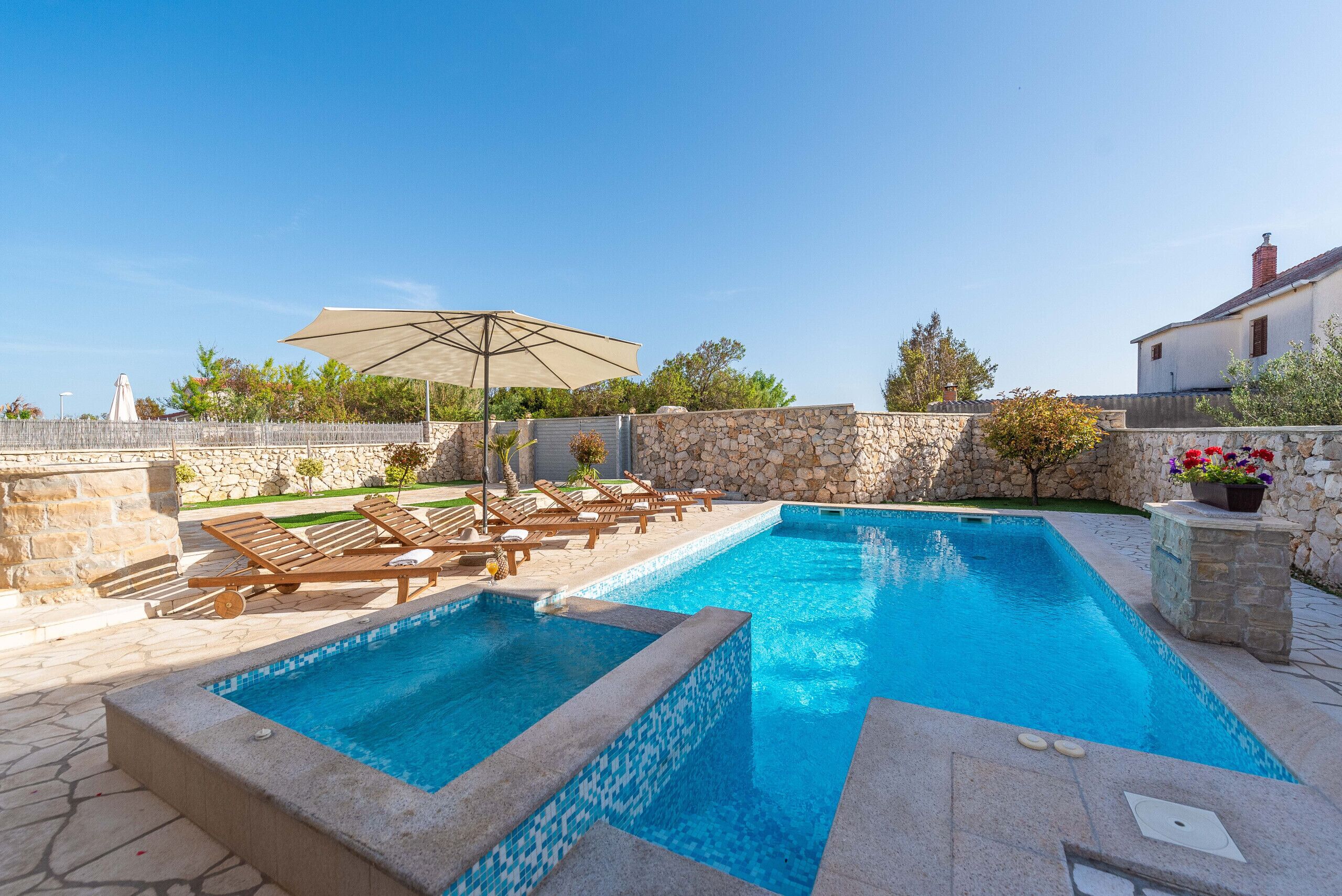 A swimming pool with lounge chairs and an umbrella, surrounded by stone walls and greenery.