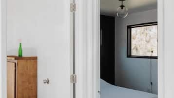 A bedroom with a bed, a window, and a door leading to another room.