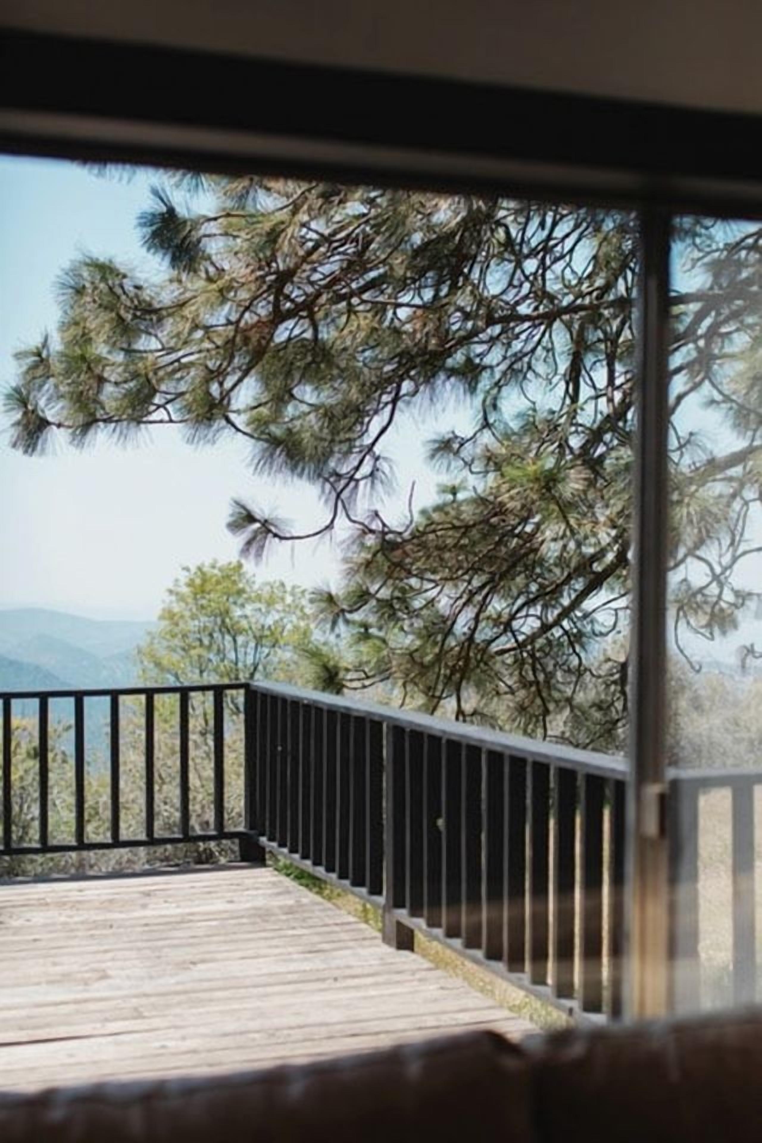 A wooden deck with a metal railing, overlooking a mountainous landscape with pine trees.