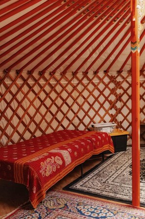 A traditional yurt interior with a bed, rugs, and a wooden lattice wall.