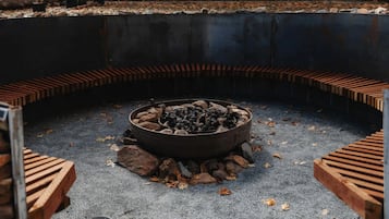 A circular fire pit with logs and rocks, surrounded by a concrete border with wooden steps.