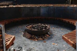 A circular fire pit with logs and rocks, surrounded by a concrete border with wooden steps.