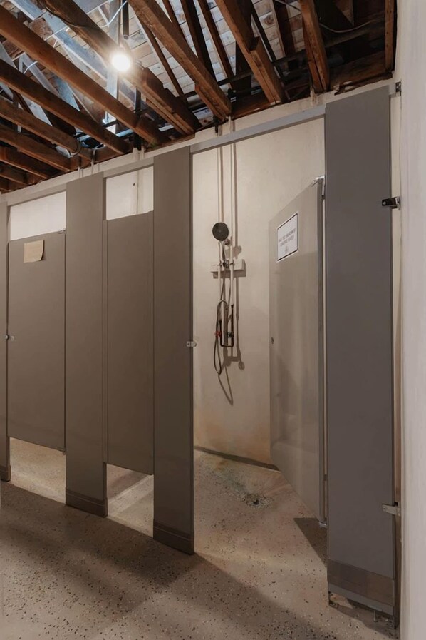 A row of restroom stalls with a shower area, including a hand dryer and a sign.