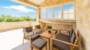 Un balcone con pareti in pietra, un tavolo e sedie in legno, una pianta in vaso e vista sul verde.