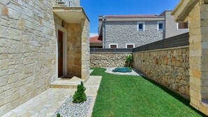 Un cortile con mura in pietra, un piccolo prato e un elemento decorativo con acqua.
