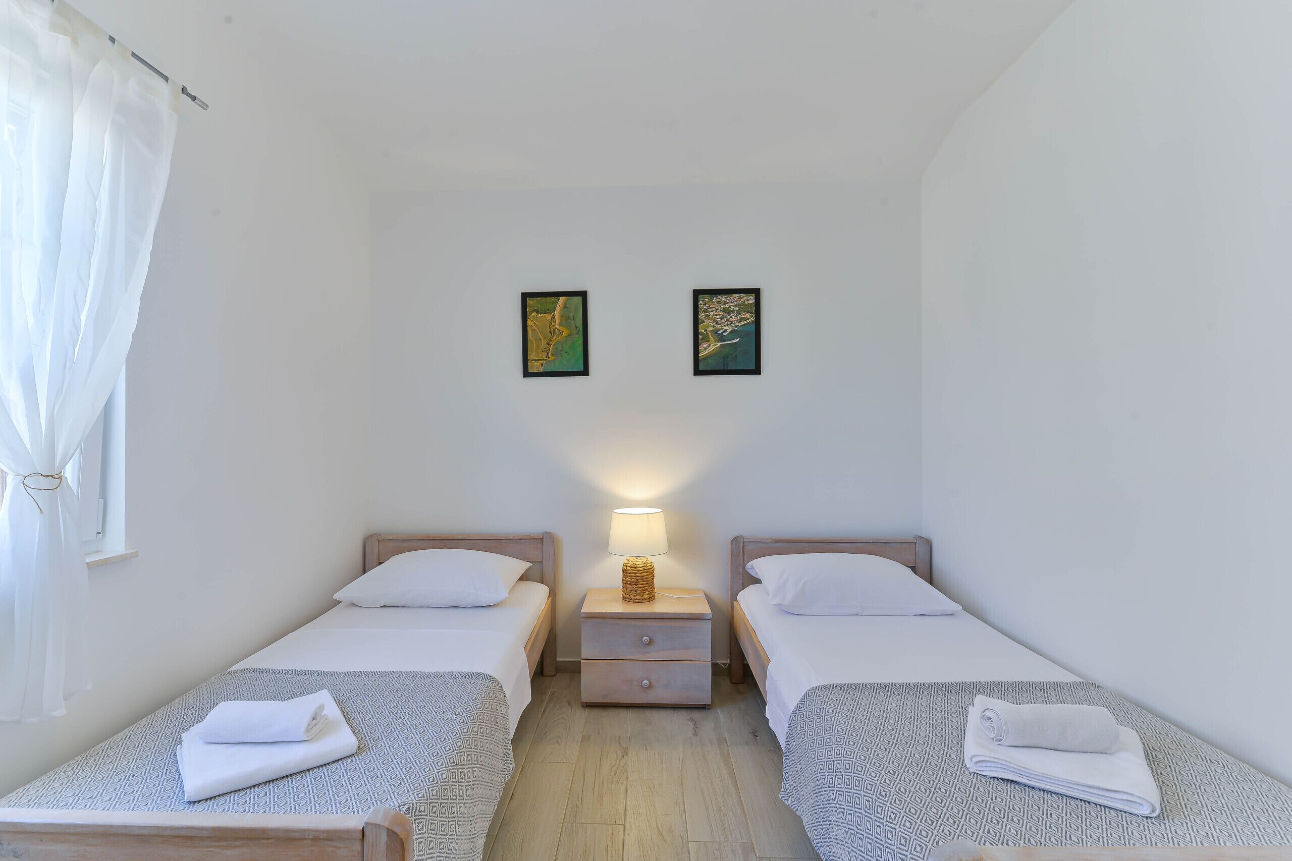 A twin room with two beds, a nightstand with a lamp, and two framed pictures on the wall.