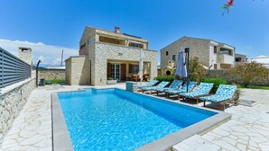 Una piscina con poltrona prendisole e un edificio in pietra.