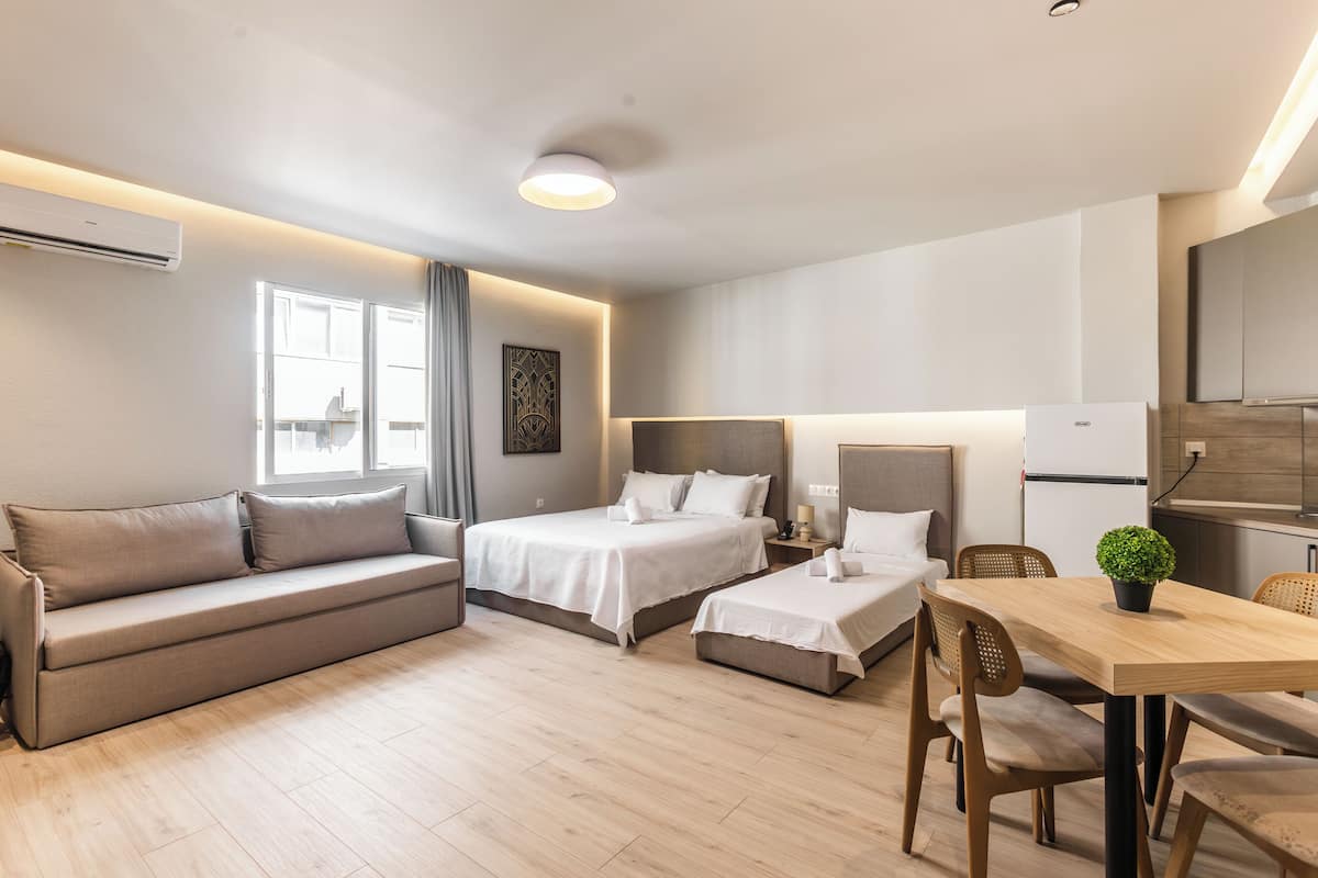 A modern hotel room with a sofa, two single beds, a wooden dining table, and a small potted plant.