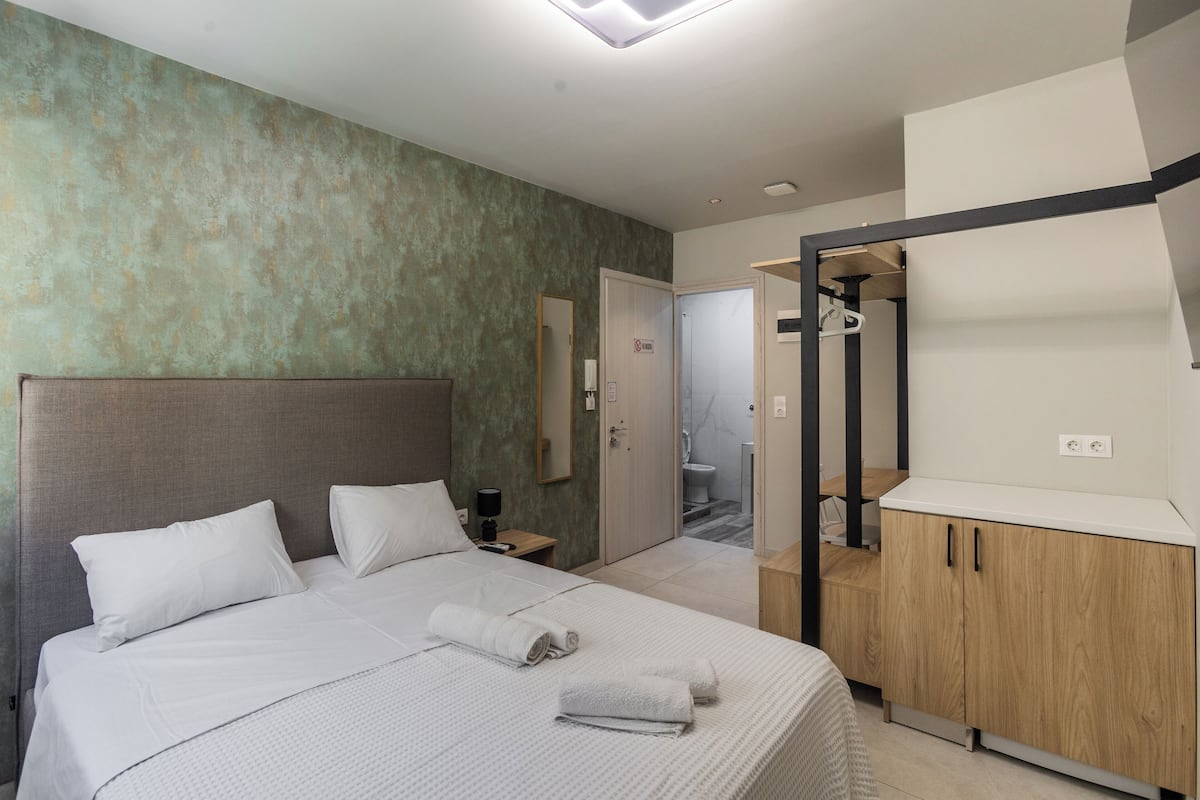 A modern hotel room with a large bed, a wooden wardrobe, and a bathroom visible through an open door.