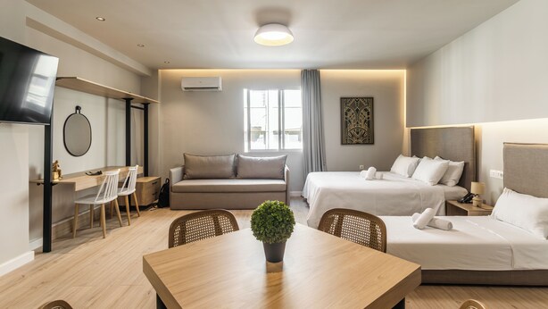 A modern hotel room with a dining area, two beds, a sofa, a TV, and a large window. - Noima Luxury Suites (Thessaloniki)