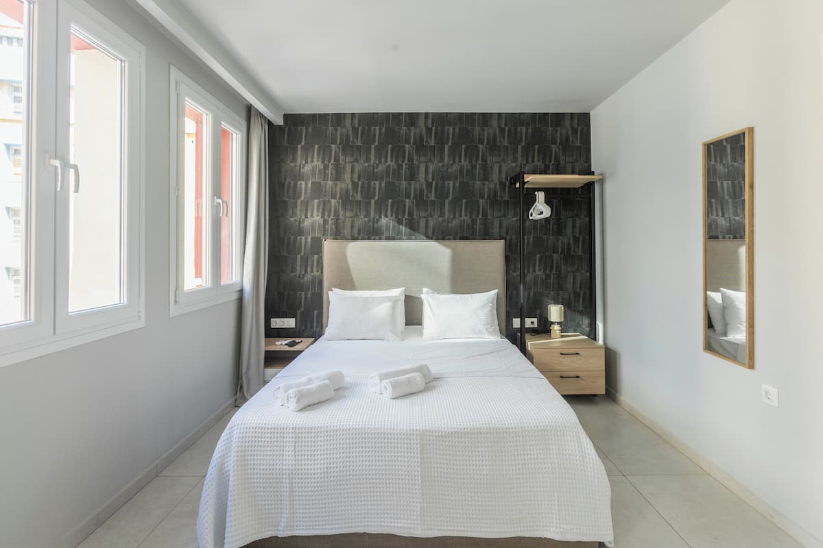 A modern hotel room with a large bed, a nightstand, a bedside lamp, and a mirror.
