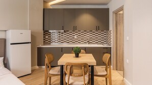 A compact kitchen with a refrigerator, a checkered backsplash, and a dining table with chairs. - Noima Luxury Suites (Thessaloniki)