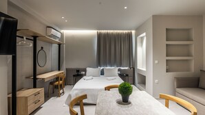 A modern hotel room with a bed, a desk, a chair, a small table, and a TV. - Noima Luxury Suites (Thessaloniki)