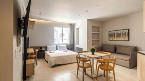 A modern hotel room with a bed, a dining table with chairs, a sofa, a TV, and a painting on the wall. - Noima Luxury Suites (Thessaloniki)
