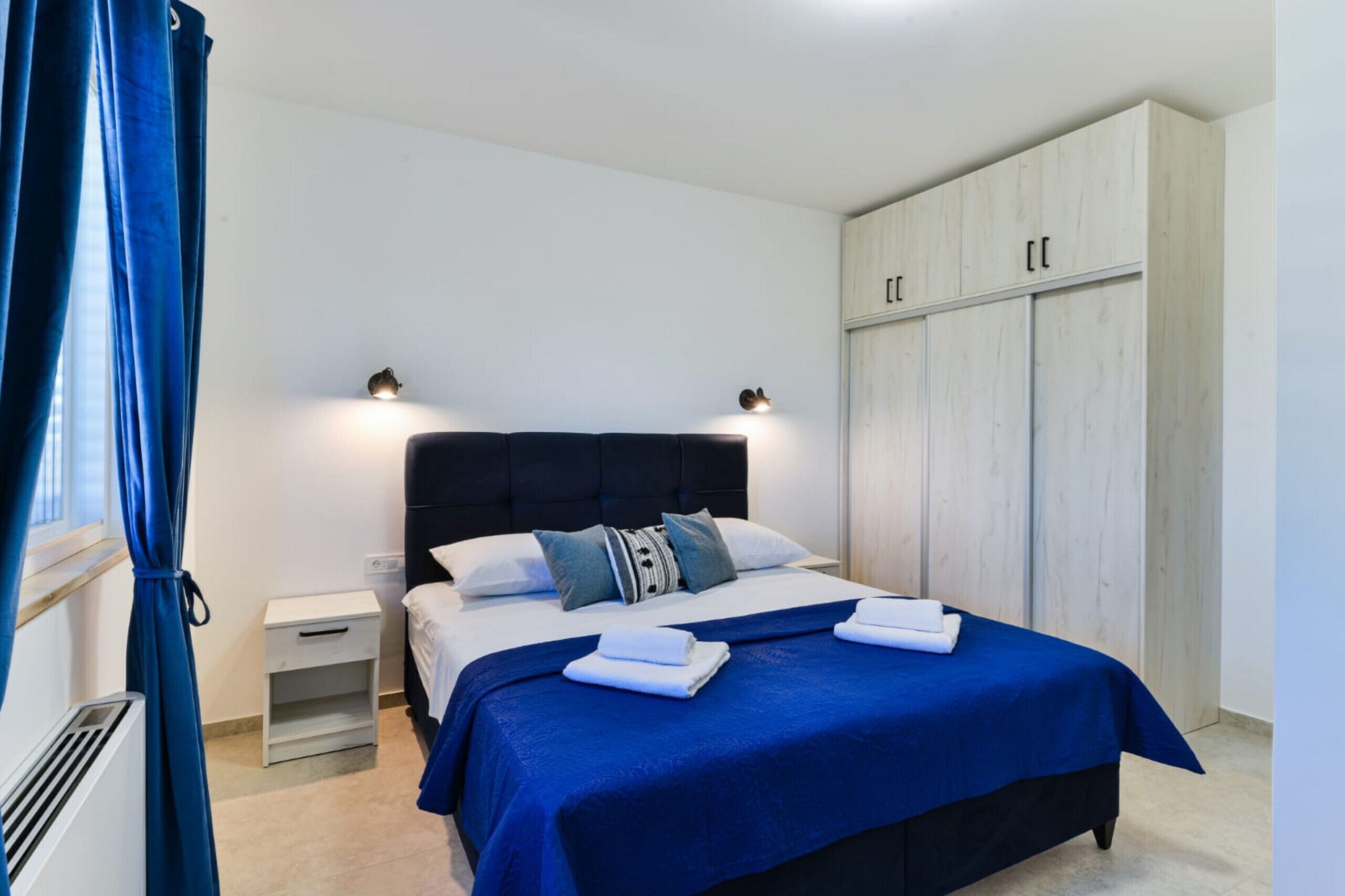 Habitación de hotel con cama, mesitas de noche, armario y ventana con cortinas.