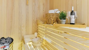A sauna with wooden walls, a stone bench, a stone basin, a woven basket with towels, a potted plant, and a bottle of wine. - Villa Rea 3 with heated pool (Privlaka)