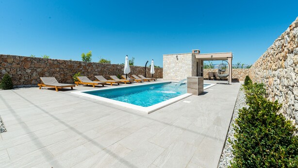 A swimming pool with lounge chairs and a stone wall. - Villa Rea 4 with heated pool (Privlaka)