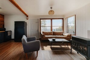 A living room with a sofa, a coffee table, a fireplace, and a large window. - Off-Grid, Rustic, Two Bedroom Cabin Nestled in the Sequoias, Perfect for a Weekend to Disconnect in Nature (Dunlap)