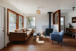 A living room with a sofa, a blue armchair, a fireplace, and large windows. - Off-Grid, Rustic, Two Bedroom Cabin Nestled in the Sequoias, Perfect for a Weekend to Disconnect in Nature (Dunlap)