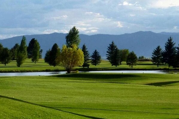 Un campo da golf con uno stagno, alberi e montagne sullo sfondo.