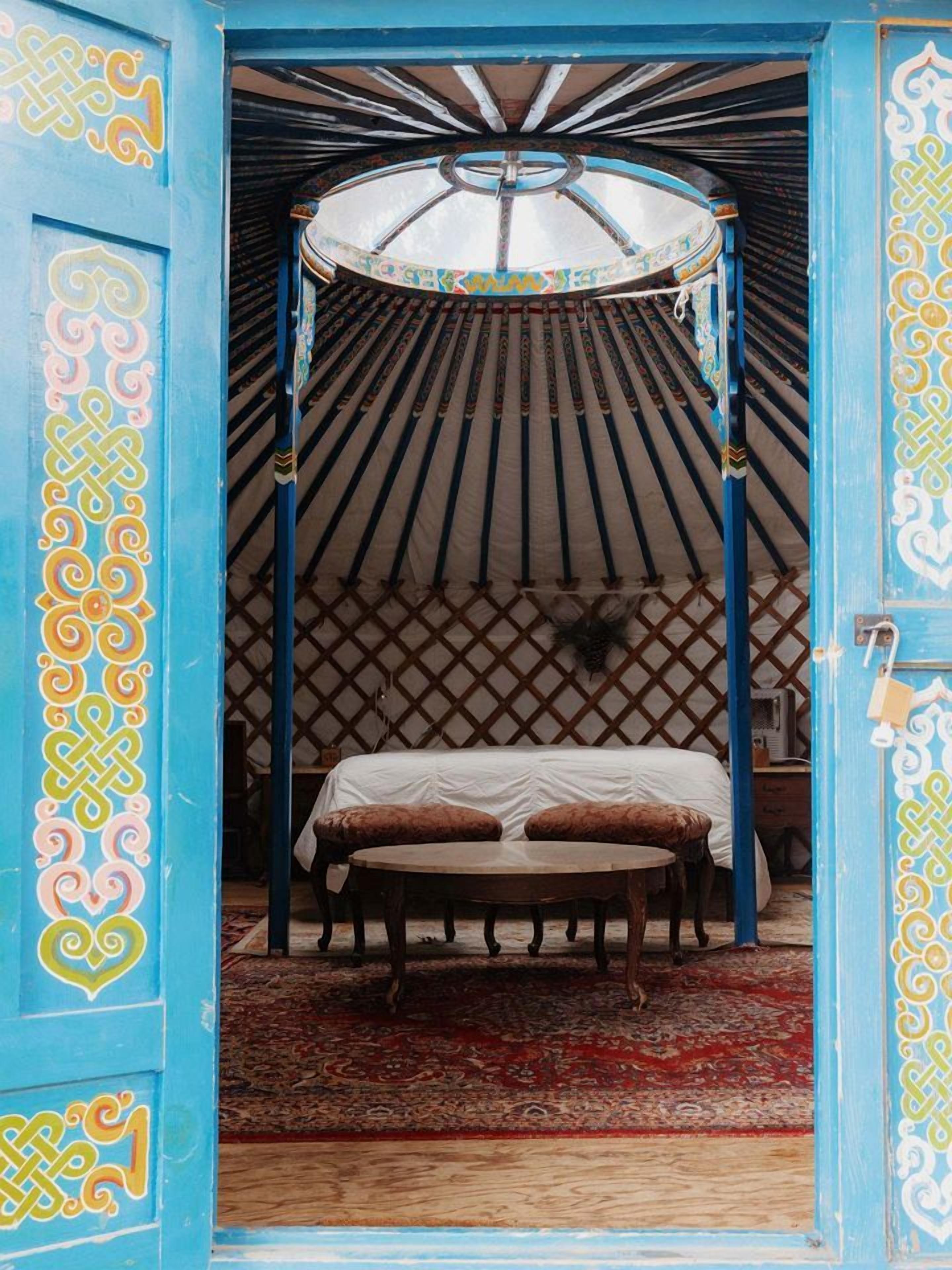 A traditional yurt with a bed, a wooden table, and a patterned rug.