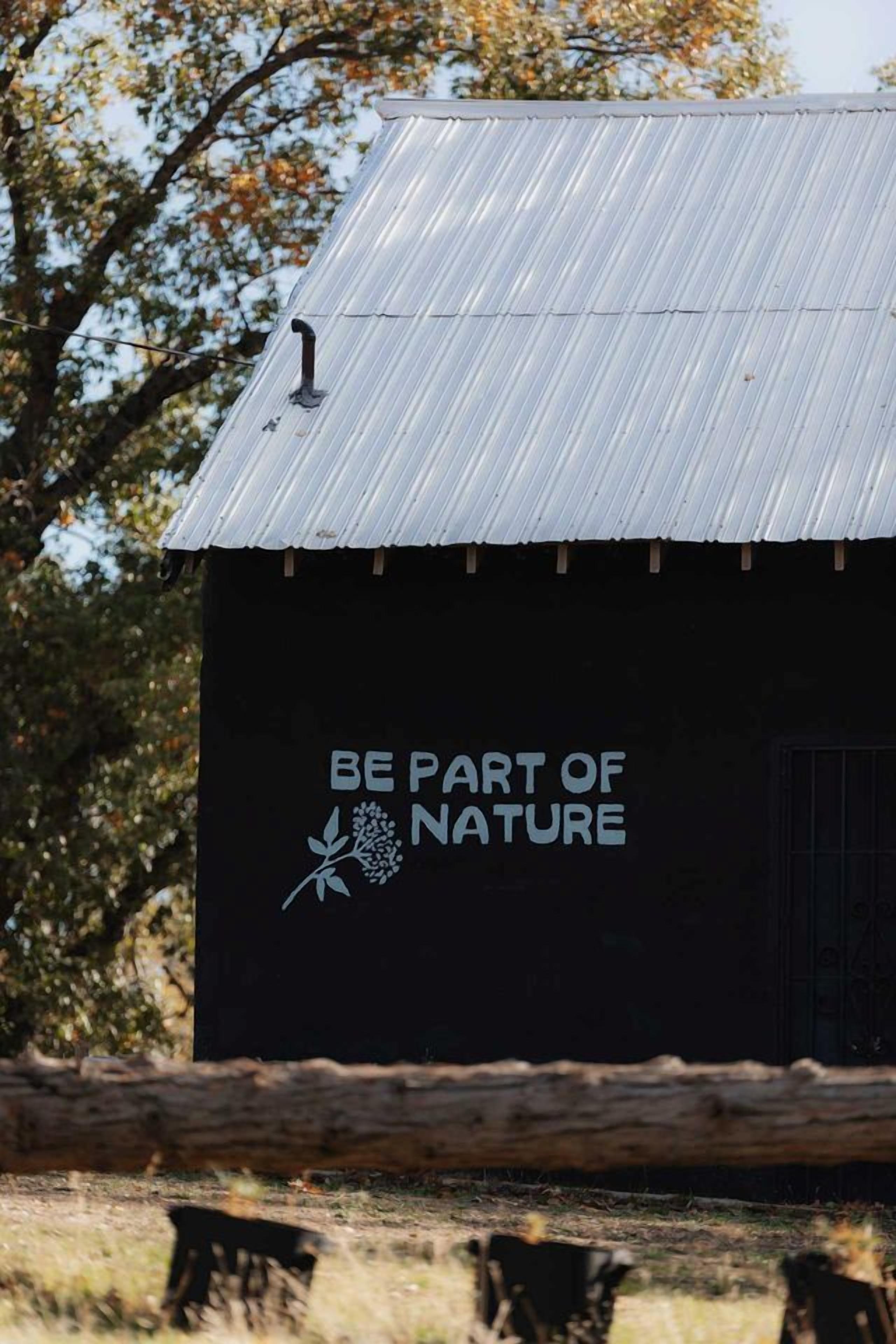 A building with a corrugated metal roof and a sign that reads 'BE PART OF NATURE.'