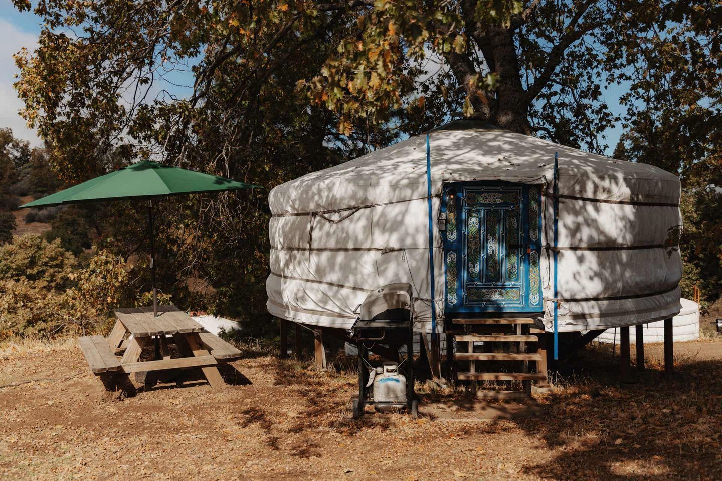 A yurt with a blue door, a picnic table, and a green umbrella.