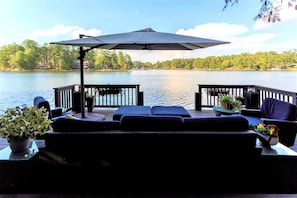 Eine Terrasse mit Gartenmöbeln, einem großen Sonnenschirm und Blick auf einen See.