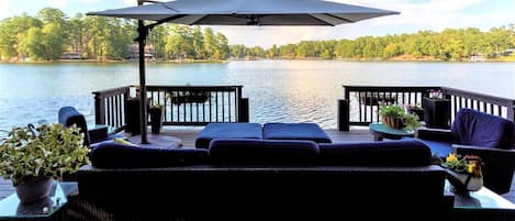 Una terraza con mobiliario exterior, un paraguas grande y vistas a un lago.