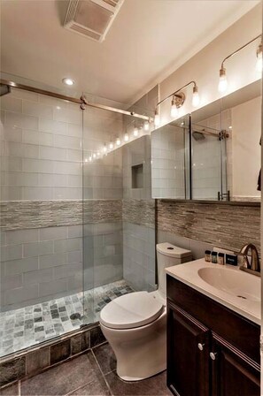 Un baño moderno con cabina de ducha de vidrio, inodoro y tocador con espejo.