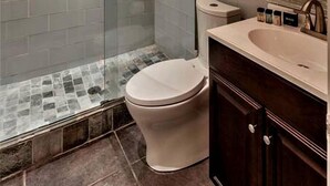 Moderni kylpyhuone, jossa on lasiseinällä varustettu suihku, wc ja peilillä varustettu pesuallas.