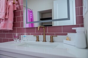 A bathroom with a white sink, a gold faucet, and a mirror reflecting a pink towel.