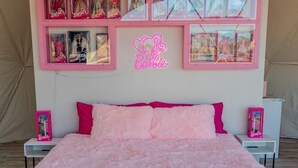 A bedroom with a pink bedspread, a neon sign, and a wall display of framed pictures.