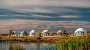 A row of geodesic dome structures by a body of water with a cloudy sky.