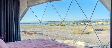 A tented room with a bed, curtains, and a view of a landscape.