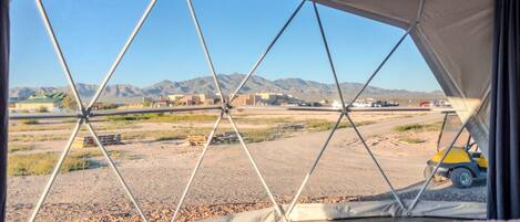 A tent with a view of a desert landscape, mountains, and a few buildings.
