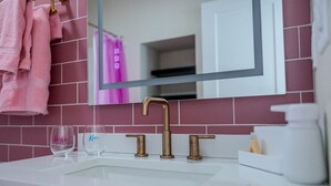 A bathroom with a white sink, a gold faucet, and a mirror reflecting a pink towel.