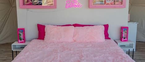 Un dormitorio con una colcha rosa, un letrero de neón y una composición de cuadros en la pared.