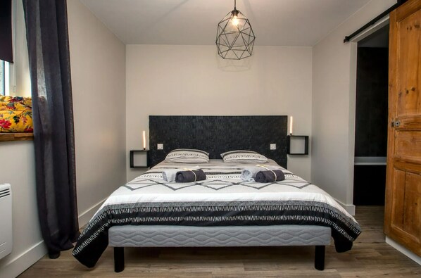 A bedroom with a bed, a geometric pendant light, bedside lamps, and a wooden wardrobe. - Relaxation by the sea - beach access - private spa and sauna (Plouescat)