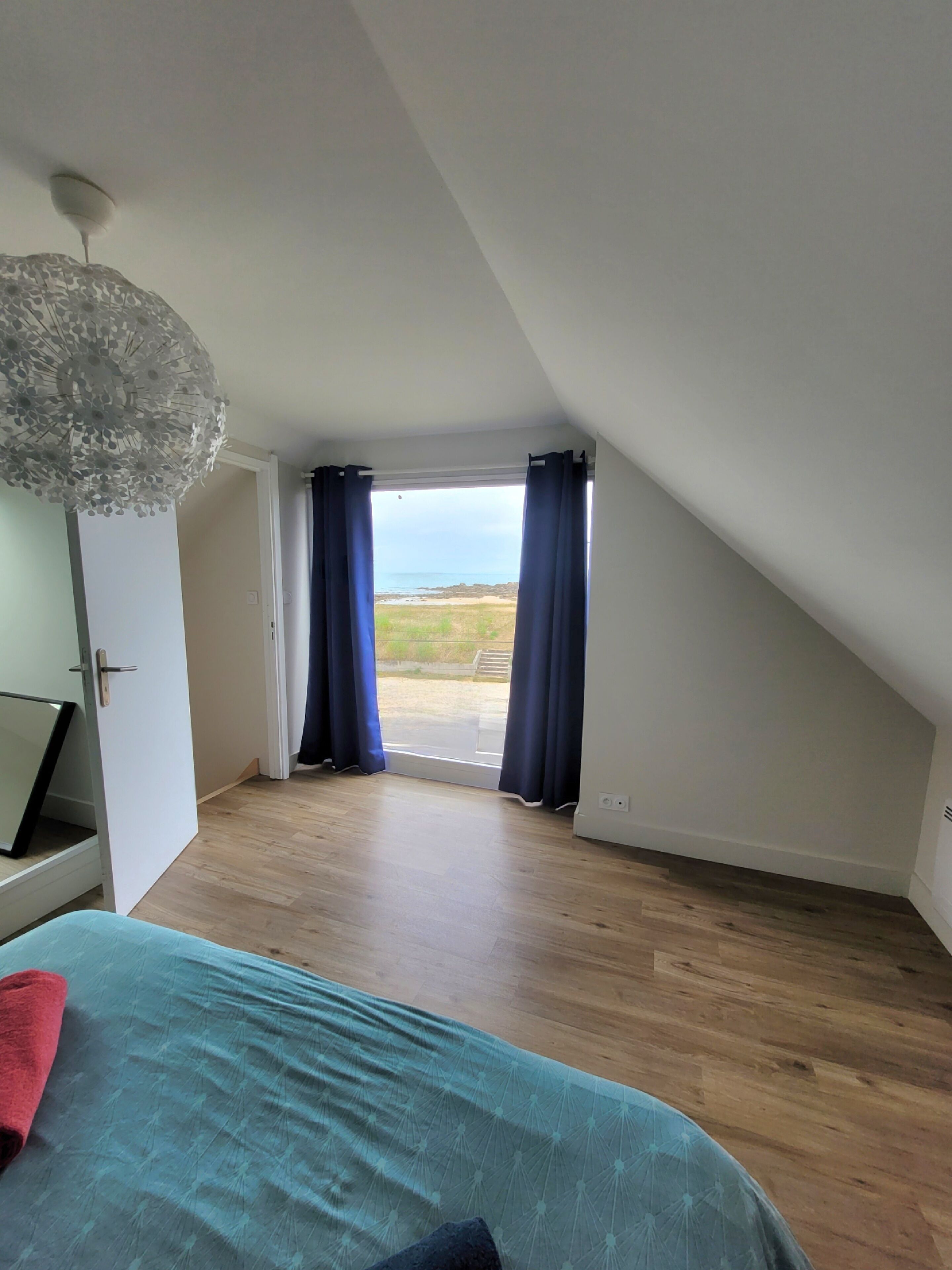 Ein Schlafzimmer mit Bett, Schreibtisch, Lampe und Meerblick durch das Fenster.