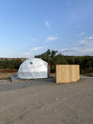 Une tente en forme de dôme géodésique, avec une structure en bois à côté.