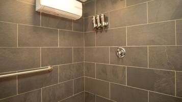 A shower with a handrail, a wall-mounted air conditioning unit, and a corner tile design.
