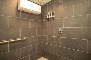 Une douche équipée d’une barre d’appui, un climatiseur fixé au mur et un motif de carrelage décoratif dans un coin.