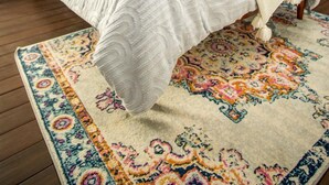 Un dormitorio con cama, mesita de noche, lámpara y una alfombra estampada.